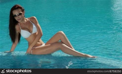 Relaxed woman wearing sunglasses and bikini by swimming pool