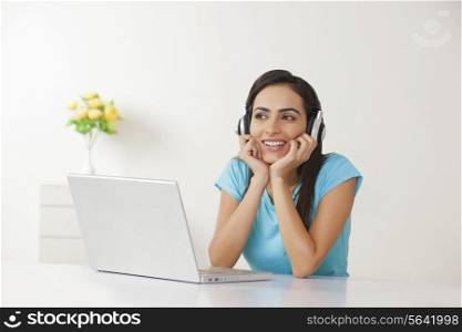 Relaxed woman with laptop listening to headphones at home