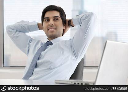 Relaxed young businessman sitting at his desk with laptop