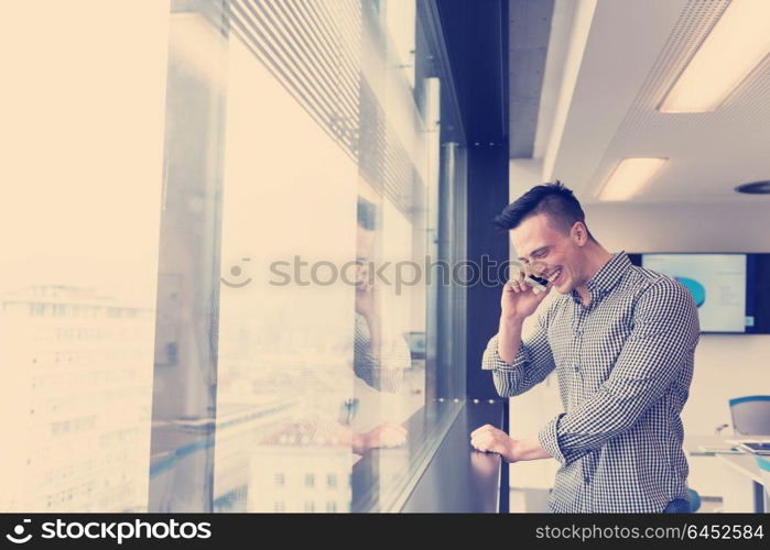 relaxed young businessman speaking on smart phone at modern startup business office meeting room with big window and city in backgronud