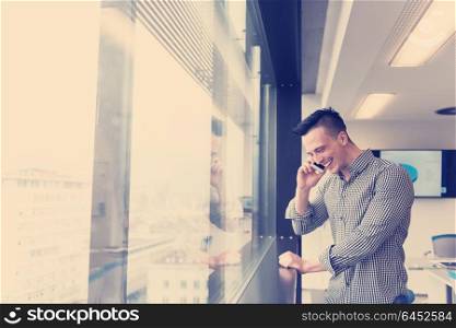 relaxed young businessman speaking on smart phone at modern startup business office meeting room with big window and city in backgronud