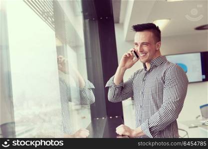 relaxed young businessman speaking on smart phone at modern startup business office meeting room with big window and city in backgronud