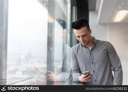 relaxed young businessman using smart phone at modern startup business office meeting room with big window and city in backgronud