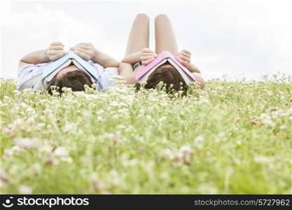 Relaxed young couple covering faces with books while lying on grass