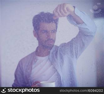 relaxed young man drink first morning coffee at modern home indoors at rainy window drops window