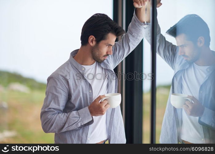 relaxed young man drink first morning coffee at modern home indoors at rainy window drops window