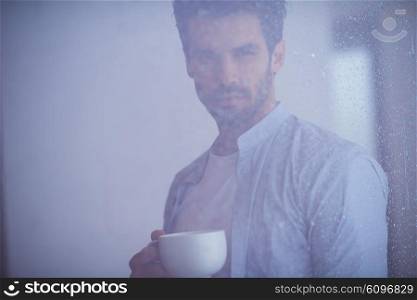 relaxed young man drink first morning coffee at modern home indoors at rainy window drops window