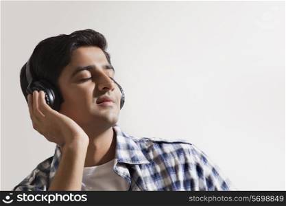 Relaxed young man listening music over colored background