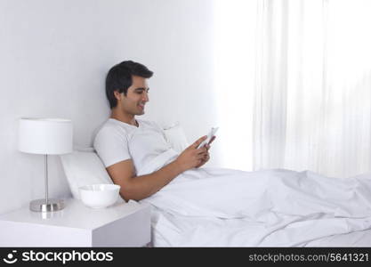 Relaxed young man using digital tablet in bed
