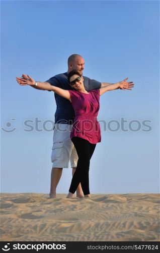 relaxed young pasionate couple enjoying the sunset beauty on their honeymoon, on a desert with orange background