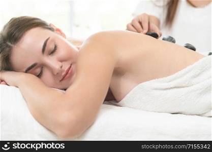 Relaxed young woman at the luxury wellness spa.. Hot stone massage treatment by therapist in spa.