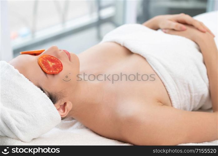 Relaxed young woman at the luxury wellness spa.. Woman getting eye nature treatment by tomato.