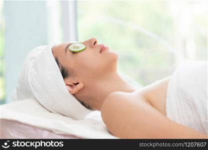 Relaxed young woman getting eye nature treatment by cucumber at luxury spa resort. Wellness and healing concept.. Woman getting eye nature treatment by cucumber.
