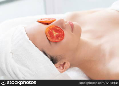 Relaxed young woman getting eye nature treatment by tomato at luxury spa resort. Wellness and healing concept.. Woman getting eye nature treatment by tomato.