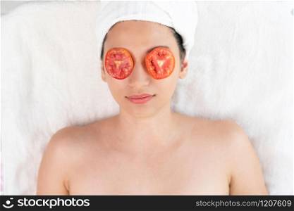 Relaxed young woman getting eye nature treatment by tomato at luxury spa resort. Wellness and healing concept.. Woman getting eye nature treatment by tomato.