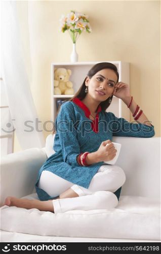 Relaxed young woman holding coffee cup in living room
