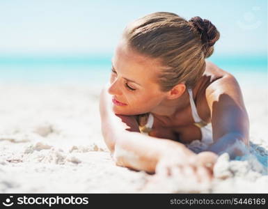 Relaxed young woman in swimsuit laying on sandy beach