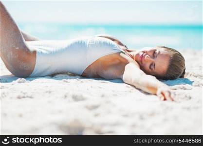 Relaxed young woman in swimsuit sunbathing on sandy beach