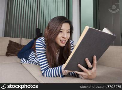 Relaxed young woman reading book at home