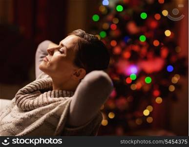 Relaxed young woman sitting in armchair in front of christmas tree