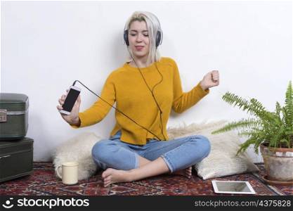 Relaxed young woman sitting on the floor at home listening to music