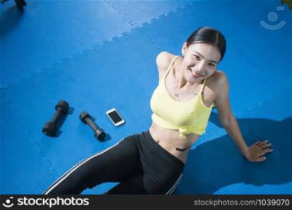 Relaxing after training. Top view of beautiful young woman sitting on exercise mat at gym