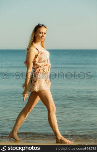 Relaxing during summertime, traveling, vacation concept. Woman in summer dress walking on beach near sea, beautiful sunny weather.. Woman in summer dress walking on beach