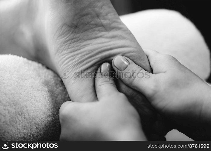Relaxing foot massage, hands of a female massage therapist massaging female client’s foot.