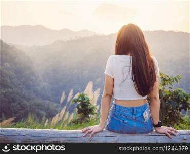 Relaxing in nature concept from backside of hipster girl sitting with enjoying the sunset on peak mountains in tropical rain forest.