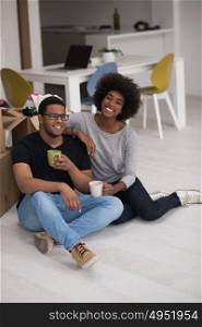 Relaxing in new house. Cheerful young African American couple sitting on the floor and drinking coffee while cardboard boxes laying all around them