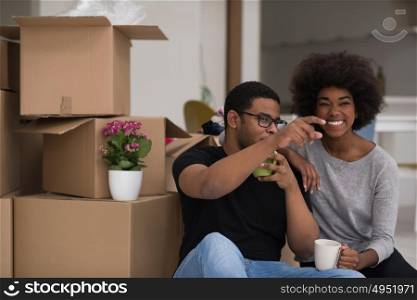 Relaxing in new house. Cheerful young African American couple sitting on the floor and drinking coffee while cardboard boxes laying all around them