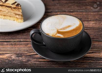 Relaxing latte coffee in black porcelain cup on wooden table