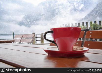 Relaxing moment with a hot cup of coffee, on a table, at an Austrian restaurant, in Hallstatt, with a view over the Dachstein Mountains, while outside is snowing heavily.