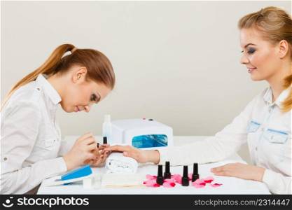 Relaxing time and wellness day concept. Blonde elegant woman visiting professional manicurist salon. Beautician makes perfect nails to client.. Beautician with client at beauty salon.
