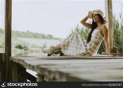 Relaxing young woman sitting on wooden pier at the calm lake