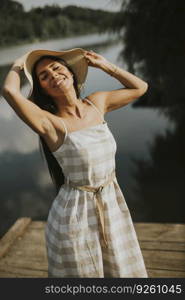 Relaxing young woman standing on wooden pier at the calm lake