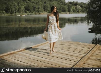 Relaxing young woman standing on wooden pier at the calm lake