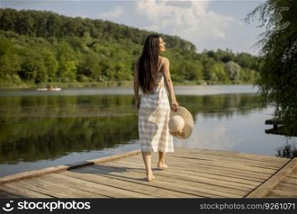 Relaxing young woman standing on wooden pier at the calm lake
