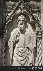 Relief sculpture of bearded male figure standing with book and holding up two fingers.