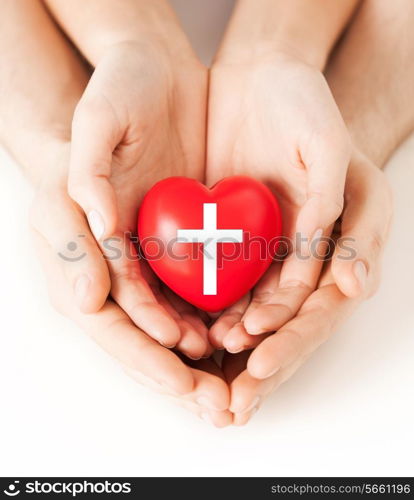 religion, christianity and charity concept - family couple hands holding red heart with christian cross symbol