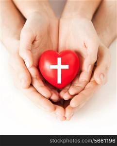 religion, christianity and charity concept - family couple hands holding red heart with christian cross symbol
