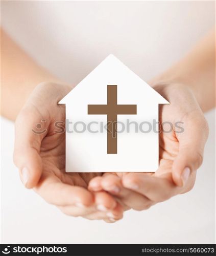 religion, christianity and charity concept - female hands holding paper house with christian cross symbol