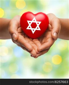 religion, christianity, jewish community and charity concept - close up of female hands holding red heart with star of david symbol over green lights background