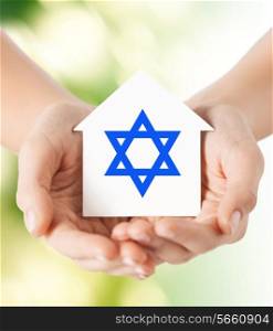 religion, judaism and charity concept - close up of woman hands holding house with star of david over green background