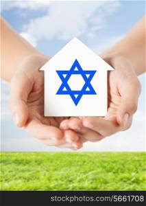 religion, judaism and charity concept - close up of woman hands holding house with star of david over blue sky with grass background