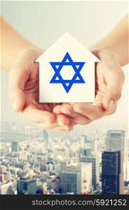 religion, judaism and charity concept - close up of woman hands holding house with star of david over city background