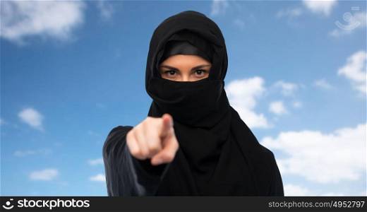 religious and people concept - muslim woman in hijab pointing finger to you over blue sky and clouds background. muslim woman in hijab pointing finger to you