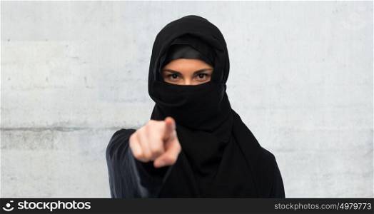 religious and people concept - muslim woman in hijab pointing finger to you over gray concrete wall background. muslim woman in hijab pointing finger to you