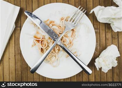 Remains of spaghetti, fork and knife on a white plate. Leftover food on a plate at the restaurant. The completion of dinner.