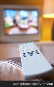 Remote control lying on armchair with television turned on in background close-up